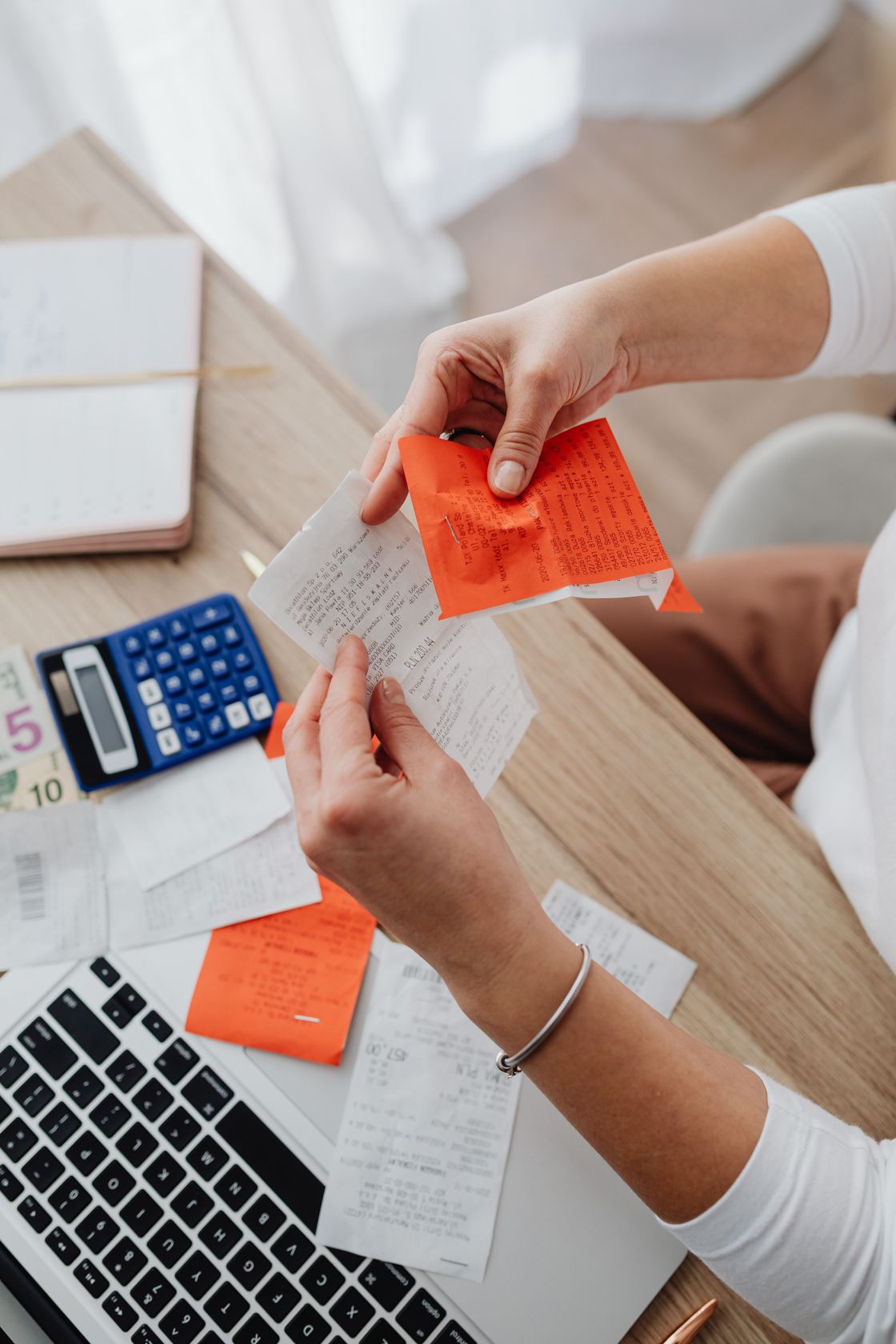 Two hands sorting through a pile of paper receipts and invoices on a desk